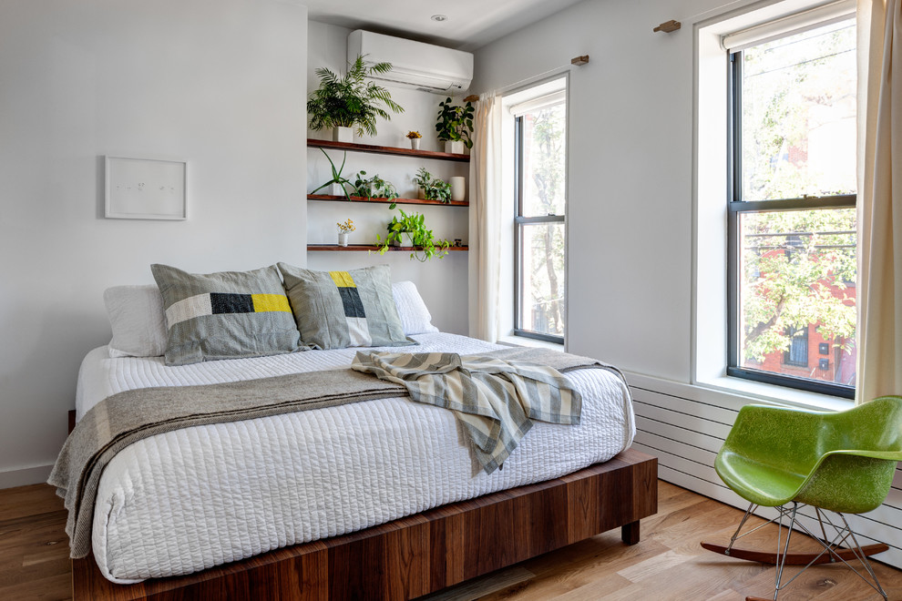 Design ideas for a mid-sized contemporary guest bedroom in New York with white walls, medium hardwood floors and brown floor.