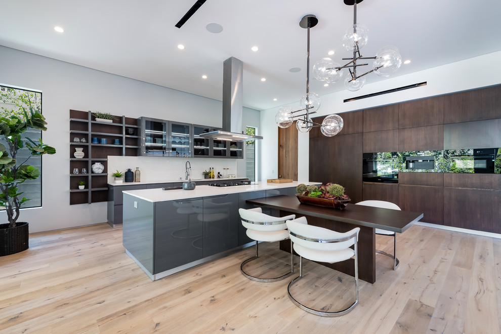 Photo of a contemporary eat-in kitchen in Los Angeles with flat-panel cabinets, dark wood cabinets, black appliances, light hardwood floors, with island, beige floor and white benchtop.