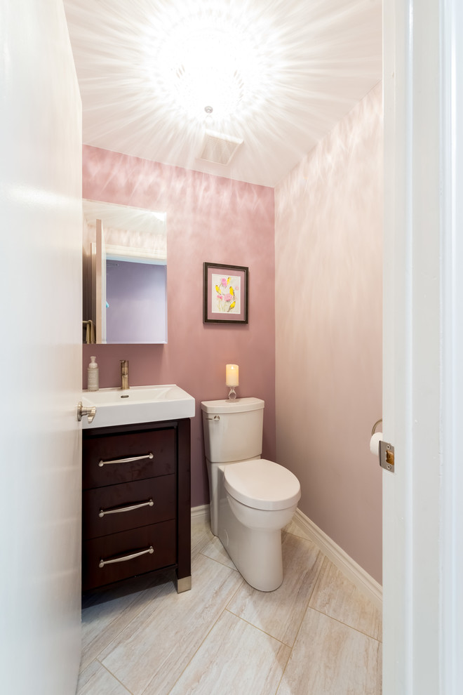 This is an example of a small transitional powder room in Ottawa with flat-panel cabinets, dark wood cabinets, a two-piece toilet, pink walls, ceramic floors, a wall-mount sink, beige tile and porcelain tile.