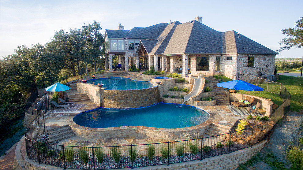 This is an example of a large transitional backyard custom-shaped infinity pool in Dallas with a water slide and natural stone pavers.
