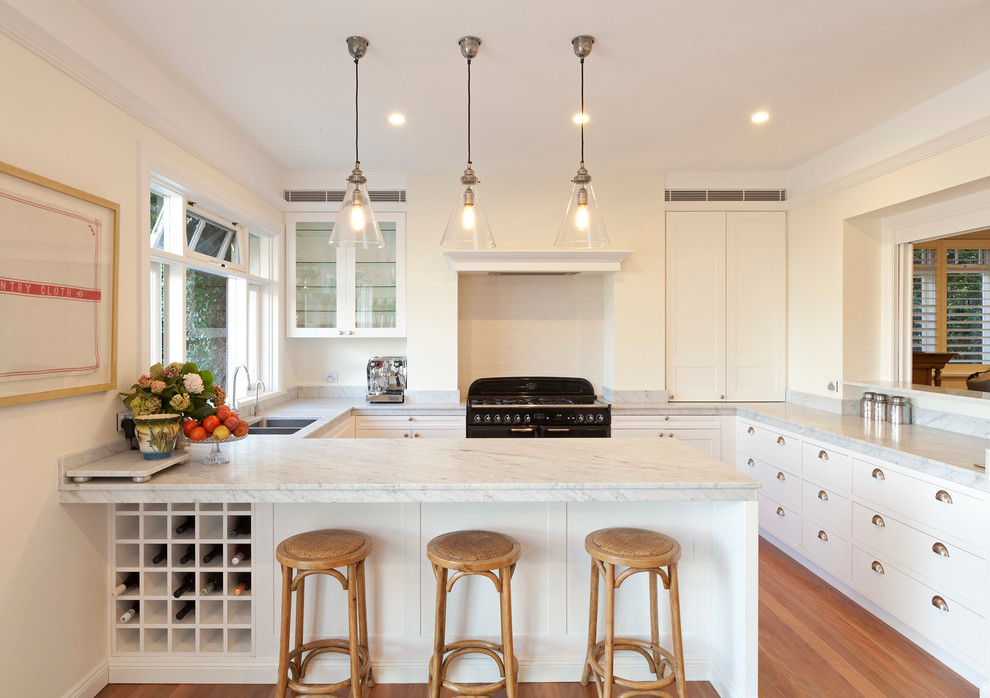 Photo of a beach style kitchen in Sydney with an undermount sink, flat-panel cabinets, white cabinets, white splashback, subway tile splashback, black appliances and a peninsula.