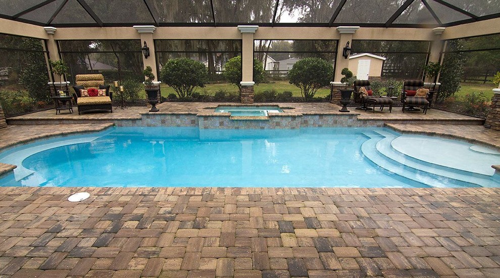 Mid-sized traditional backyard custom-shaped lap pool in Tampa with a hot tub and brick pavers.