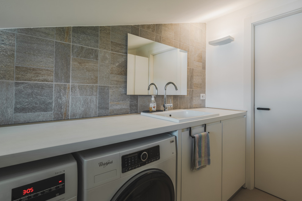 Inspiration for a mid-sized industrial galley dedicated laundry room in Milan with a drop-in sink, flat-panel cabinets, yellow cabinets, laminate benchtops, beige splashback, ceramic splashback, white walls, porcelain floors, a side-by-side washer and dryer, beige floor and white benchtop.