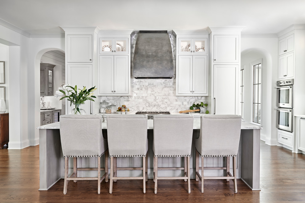 This is an example of a transitional l-shaped eat-in kitchen in Nashville with a farmhouse sink, beaded inset cabinets, white cabinets, marble benchtops, multi-coloured splashback, stone tile splashback, stainless steel appliances, dark hardwood floors and with island.