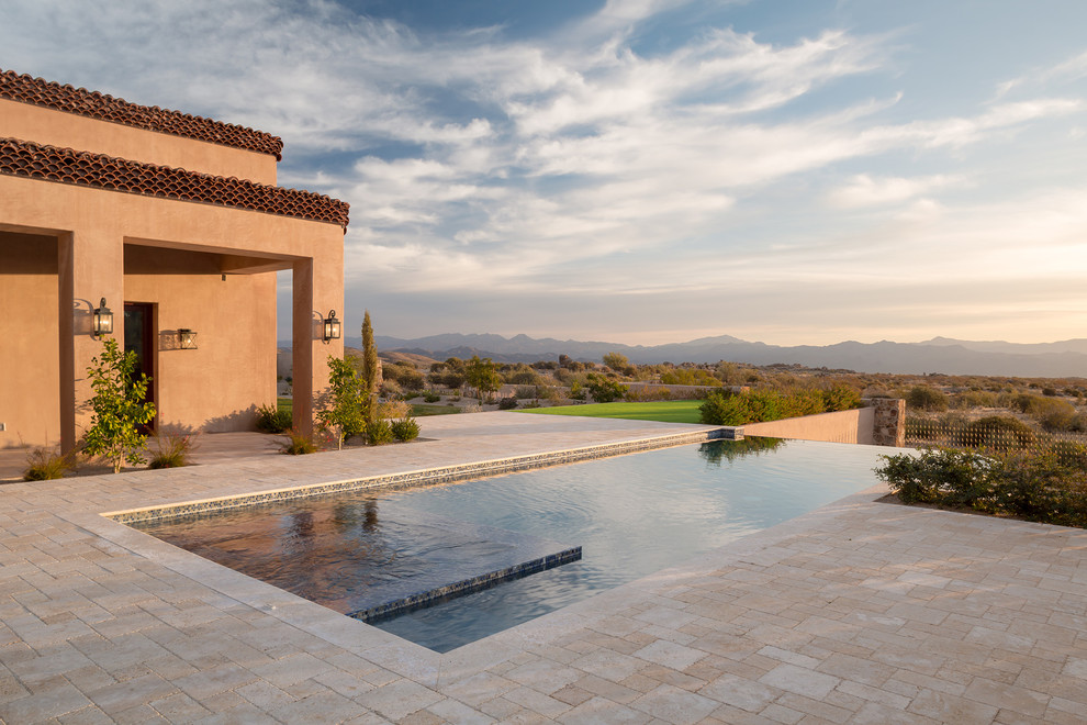 Photo of an expansive mediterranean backyard rectangular infinity pool in Phoenix with a hot tub and natural stone pavers.