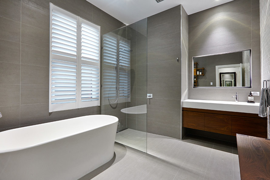 Photo of a contemporary bathroom in Melbourne with an integrated sink, flat-panel cabinets, white cabinets, solid surface benchtops, a freestanding tub, an open shower, gray tile and porcelain tile.