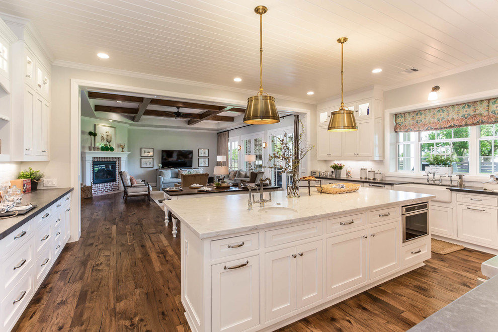 Inspiration for a country kitchen in Houston with a farmhouse sink, white cabinets, white splashback, medium hardwood floors, with island and brown floor.