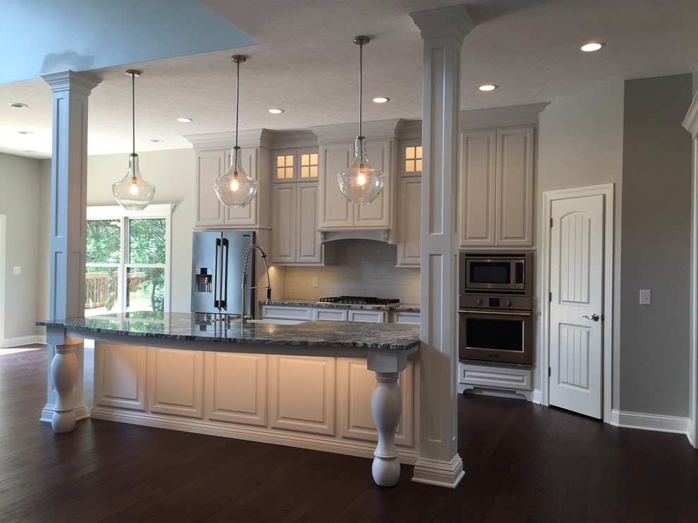 Open concept kitchen - transitional single-wall dark wood floor open concept kitchen idea with a farmhouse sink, raised-panel cabinets, white cabinets, granite countertops, white backsplash, stainless steel appliances and an island