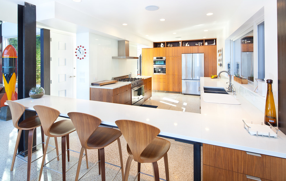 Midcentury u-shaped kitchen in Seattle with a double-bowl sink, flat-panel cabinets, medium wood cabinets, white splashback, glass sheet splashback and stainless steel appliances.