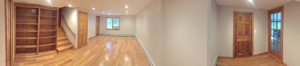 Modelo de sótano con ventanas de estilo americano con paredes beige, suelo de madera clara y suelo marrón