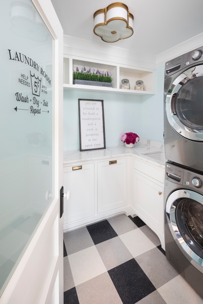 This is an example of a beach style l-shaped dedicated laundry room in Minneapolis with an undermount sink, white cabinets, blue walls, a stacked washer and dryer, multi-coloured floor and grey benchtop.