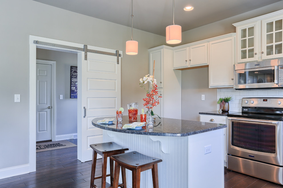Example of a large transitional l-shaped dark wood floor eat-in kitchen design with recessed-panel cabinets, white cabinets, granite countertops, white backsplash, stainless steel appliances and an island
