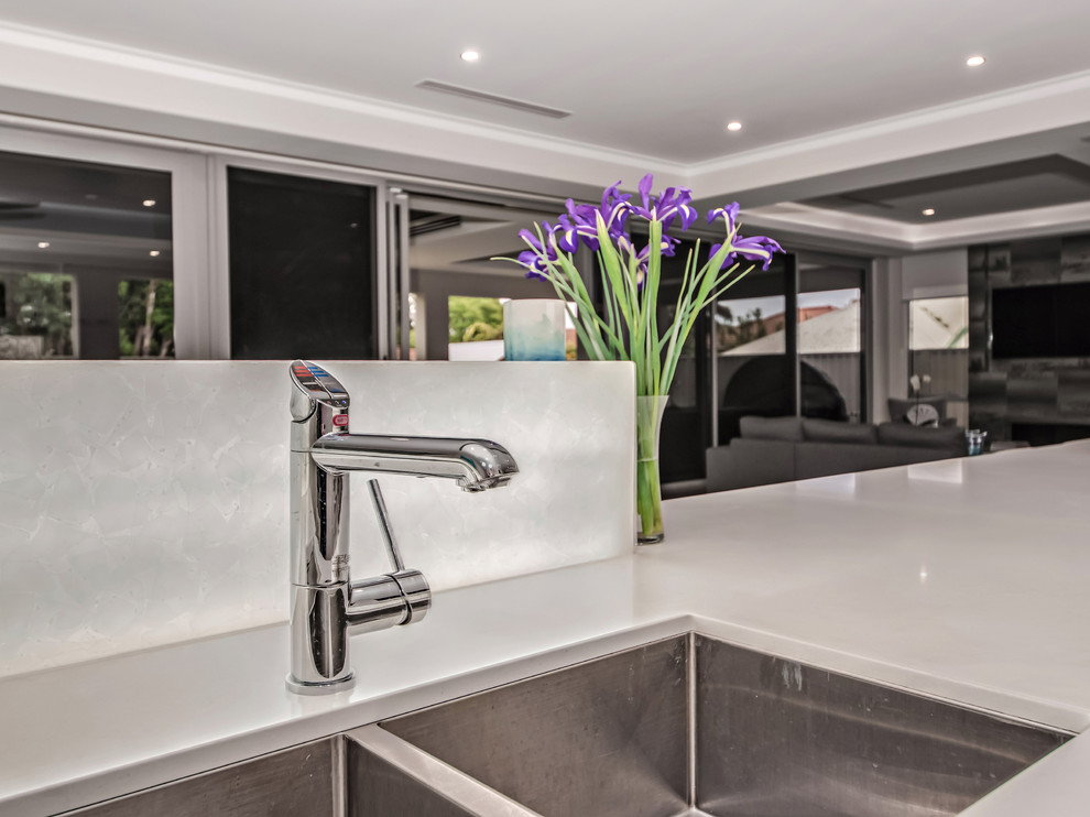 This is an example of a contemporary galley open plan kitchen in Perth with a built-in sink, flat-panel cabinets, light wood cabinets, engineered stone countertops, white splashback, glass sheet splashback, stainless steel appliances, ceramic flooring, grey floors, white worktops and a drop ceiling.