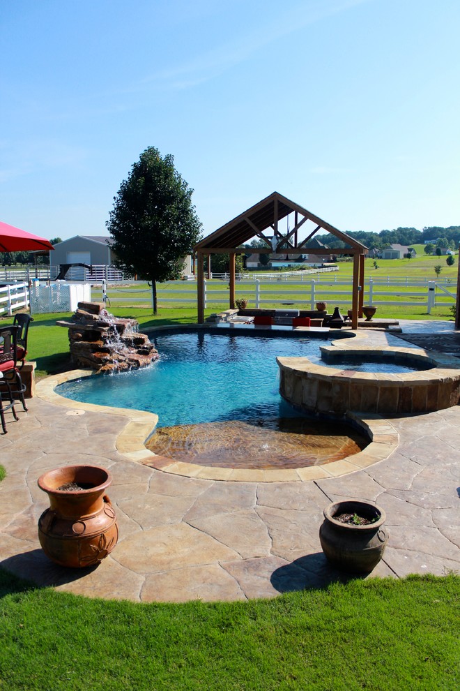 Photo of a large country backyard custom-shaped lap pool in Little Rock with a hot tub and stamped concrete.