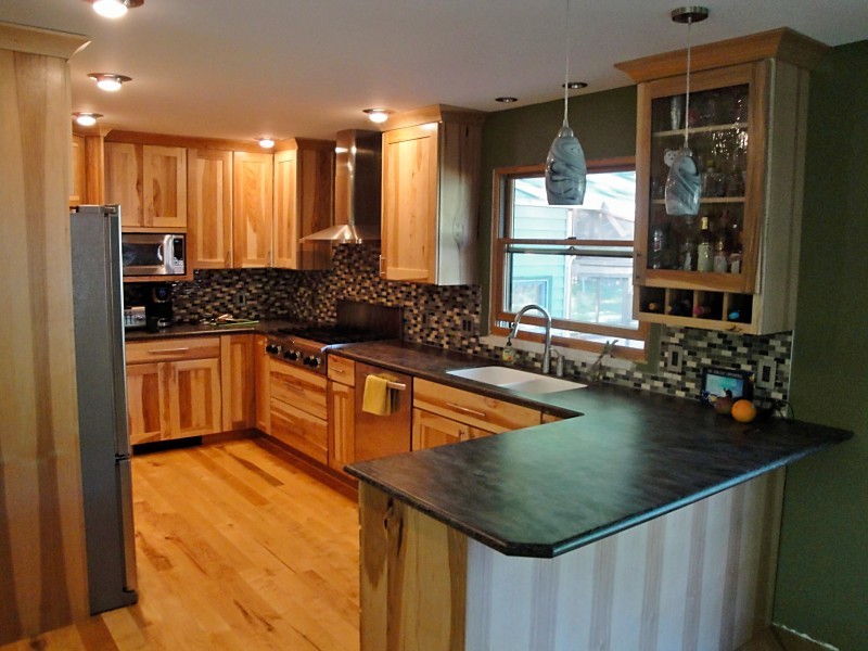 Example of a mid-sized mountain style u-shaped light wood floor eat-in kitchen design with an undermount sink, flat-panel cabinets, light wood cabinets, solid surface countertops, stainless steel appliances, a peninsula and brown countertops