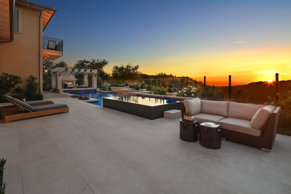 Inspiration for a large contemporary backyard custom-shaped infinity pool in Orange County with a hot tub and tile.