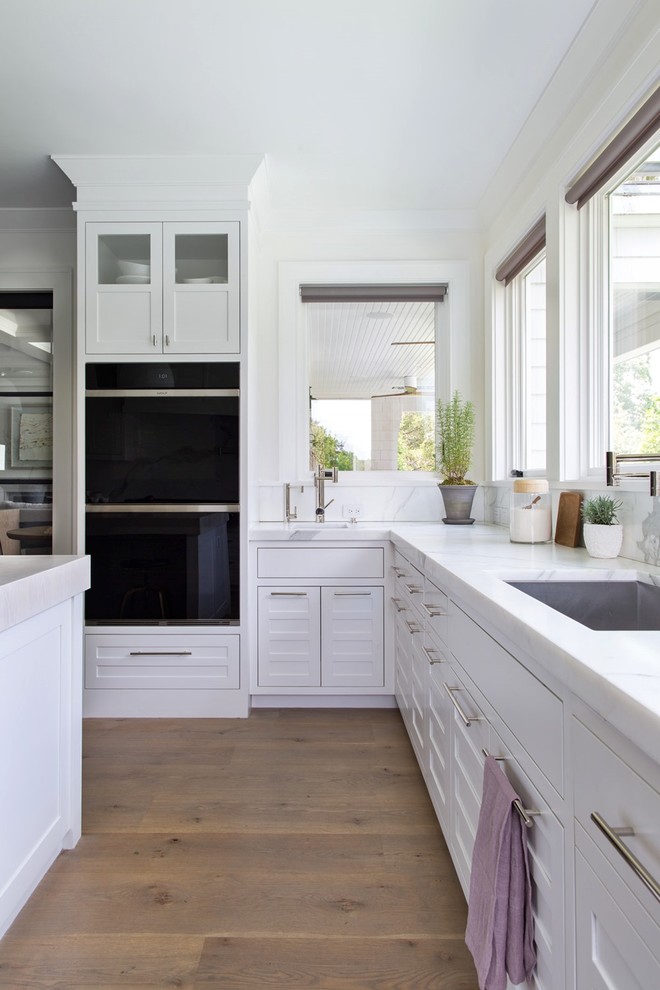 Example of a large transitional medium tone wood floor and brown floor eat-in kitchen design with an undermount sink, recessed-panel cabinets, white cabinets, marble countertops, white backsplash, marble backsplash, black appliances, two islands and white countertops