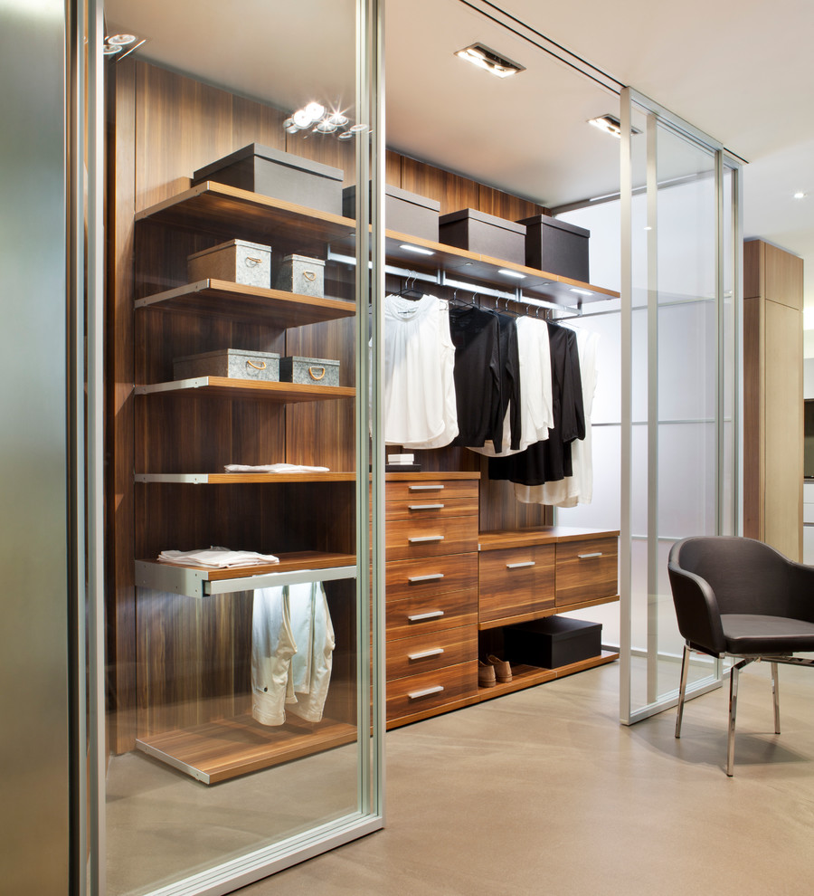 Mid-sized contemporary women's walk-in wardrobe in Madrid with glass-front cabinets, concrete floors and beige floor.