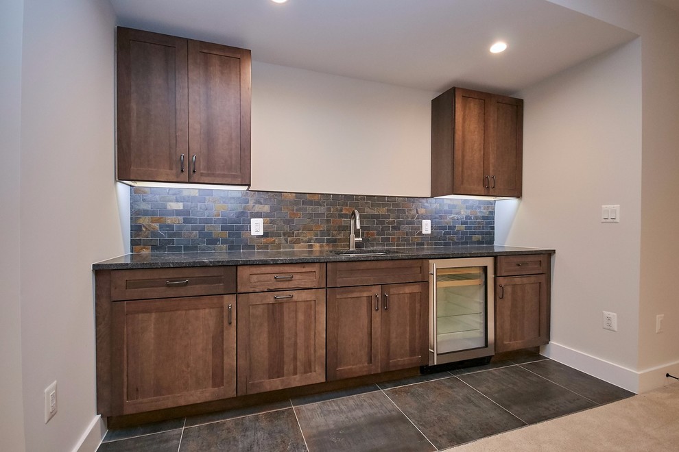 Photo of a mid-sized country galley wet bar in DC Metro with an undermount sink, shaker cabinets, medium wood cabinets, granite benchtops, multi-coloured splashback, slate splashback, ceramic floors, grey floor and grey benchtop.