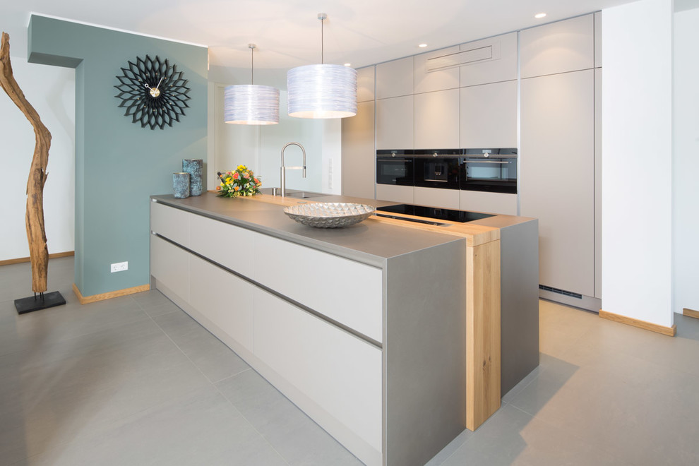 This is an example of a mid-sized contemporary galley kitchen in Dresden with black appliances, flat-panel cabinets, beige cabinets, a peninsula, beige floor and grey benchtop.