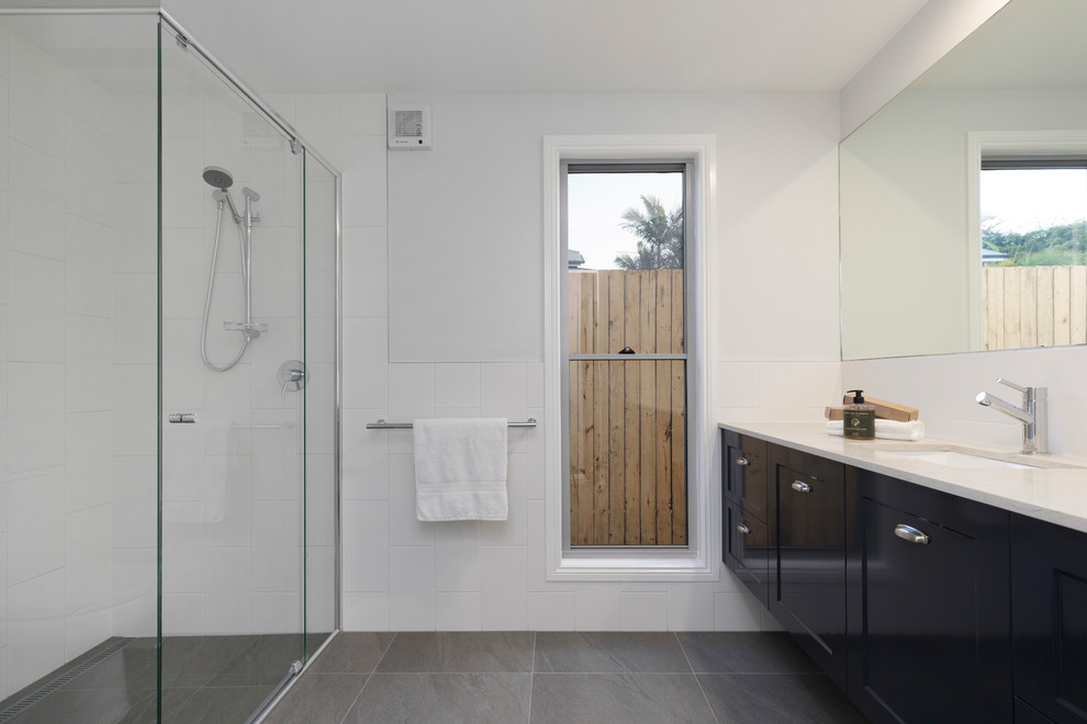 Photo of a mid-sized traditional kids bathroom in Brisbane with shaker cabinets, blue cabinets, white tile, ceramic tile, white walls, ceramic floors, a drop-in sink, granite benchtops, grey floor, a hinged shower door and white benchtops.