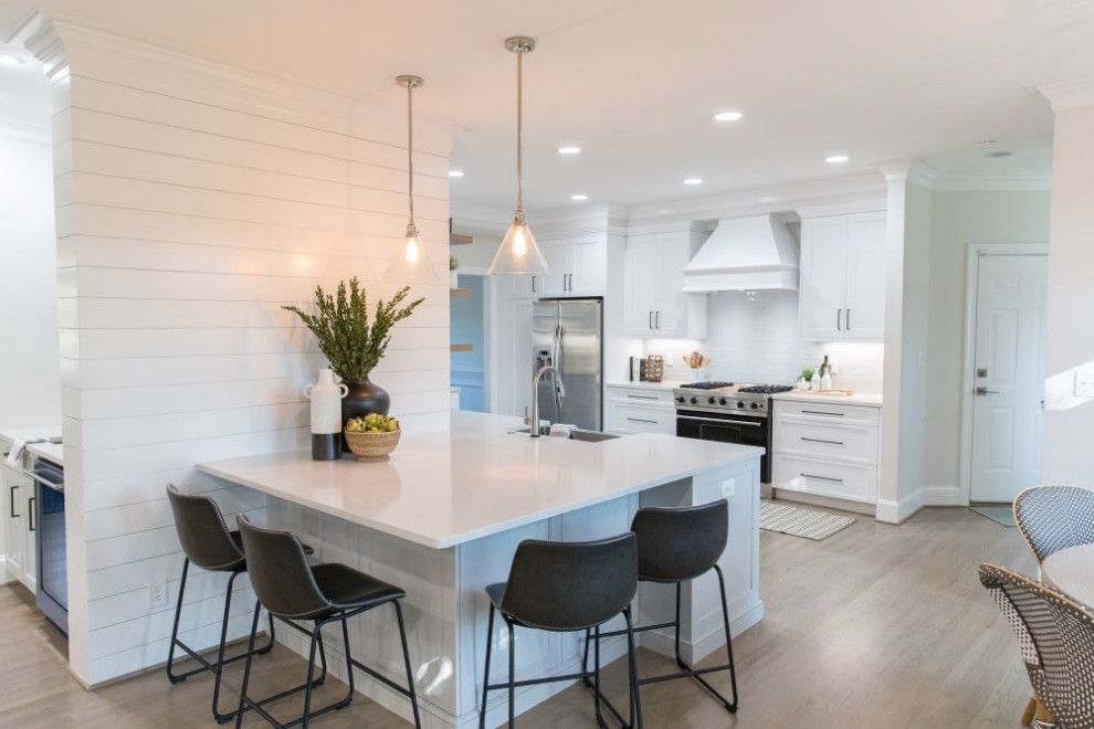 Inspiration for a mid-sized transitional u-shaped light wood floor and gray floor eat-in kitchen remodel in Charlotte with a farmhouse sink, shaker cabinets, white cabinets, quartz countertops, white backsplash, porcelain backsplash, stainless steel appliances, a peninsula and white countertops