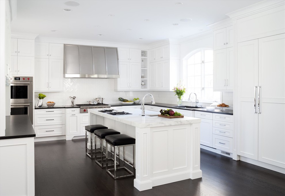 Photo of a transitional u-shaped kitchen in DC Metro with white cabinets, white splashback, dark hardwood floors, with island and brown floor.