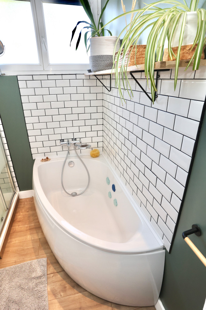 Modern inredning av ett litet badrum med dusch, med ett hörnbadkar, vit kakel, tunnelbanekakel, gröna väggar, ljust trägolv och dusch med skjutdörr