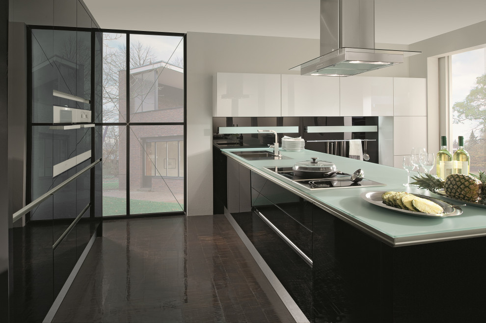 Design ideas for a mid-sized modern l-shaped eat-in kitchen in Vancouver with a drop-in sink, flat-panel cabinets, black cabinets, glass benchtops, black splashback, glass sheet splashback, stainless steel appliances, porcelain floors, a peninsula, brown floor and green benchtop.
