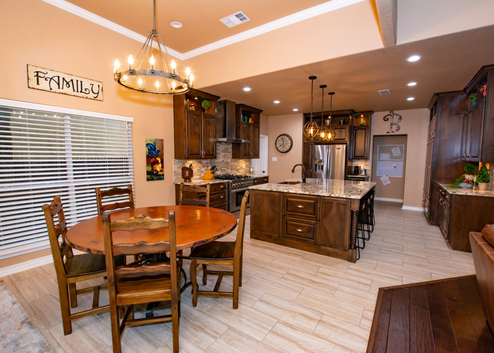 Example of a transitional porcelain tile and beige floor kitchen design in Austin with a farmhouse sink, raised-panel cabinets, dark wood cabinets, granite countertops, stone tile backsplash, stainless steel appliances and an island