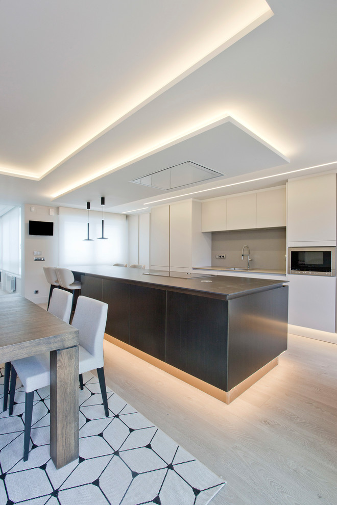 Photo of a large contemporary single-wall open plan kitchen in Other with an undermount sink, flat-panel cabinets, beige cabinets, glass benchtops, beige splashback, window splashback, stainless steel appliances, porcelain floors, with island, brown floor and beige benchtop.
