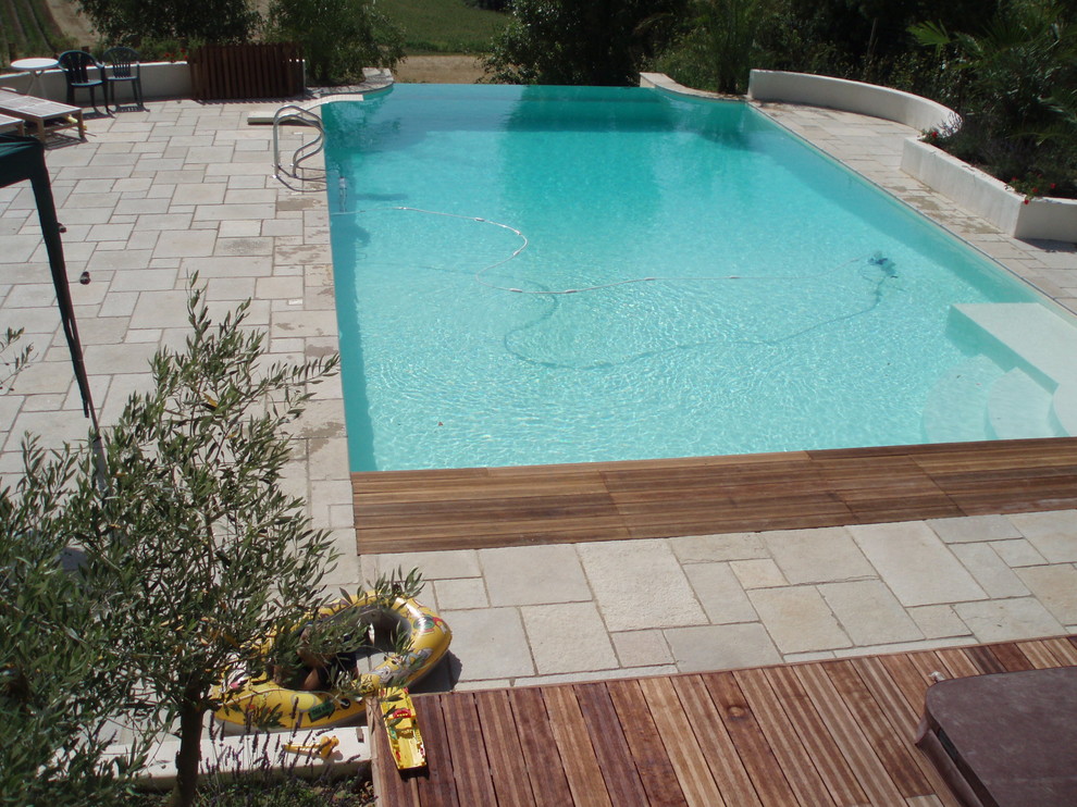 This is an example of a mid-sized mediterranean rooftop rectangular infinity pool in Bordeaux with a water feature and natural stone pavers.