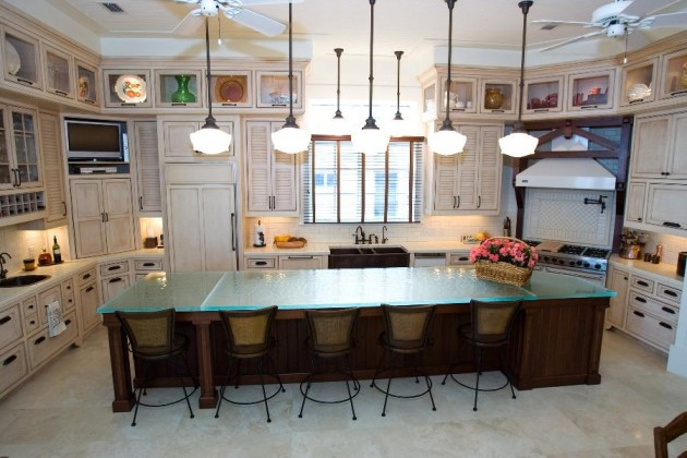 Photo of a large u-shaped kitchen in Austin with a triple-bowl sink, louvered cabinets, distressed cabinets, glass benchtops, beige splashback, stone tile splashback, panelled appliances, porcelain floors, with island, beige floor and blue benchtop.