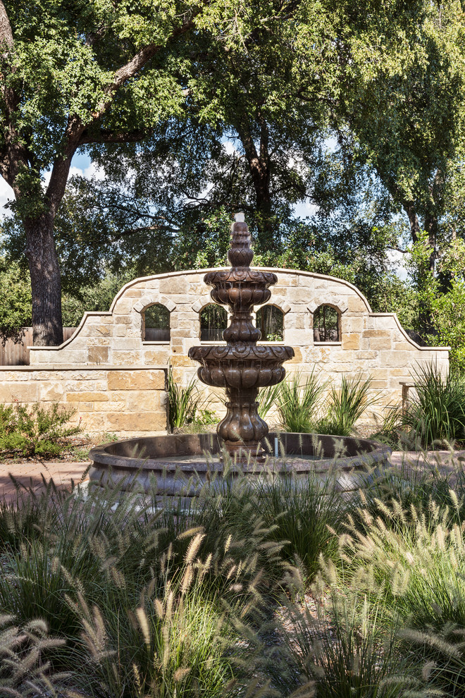 This is an example of a small courtyard full sun formal garden for summer in Austin with a water feature and natural stone pavers.
