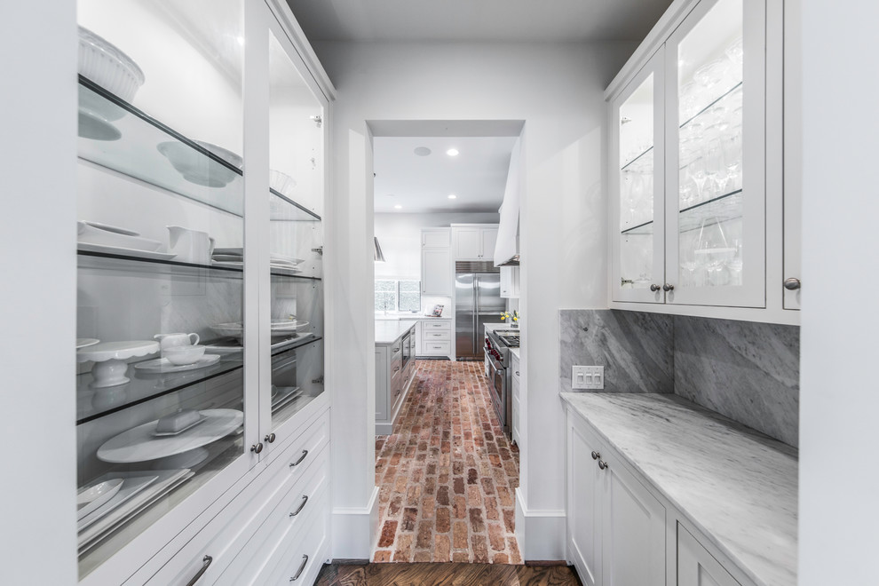 Photo of a large mediterranean u-shaped eat-in kitchen in Houston with a double-bowl sink, raised-panel cabinets, white cabinets, marble benchtops, white splashback, marble splashback, stainless steel appliances, brick floors, with island and white floor.
