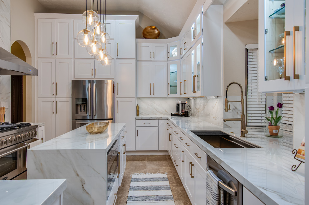 Large modern l-shaped eat-in kitchen in Houston with an undermount sink, shaker cabinets, white cabinets, solid surface benchtops, white splashback, porcelain splashback, stainless steel appliances, marble floors, with island, beige floor and white benchtop.