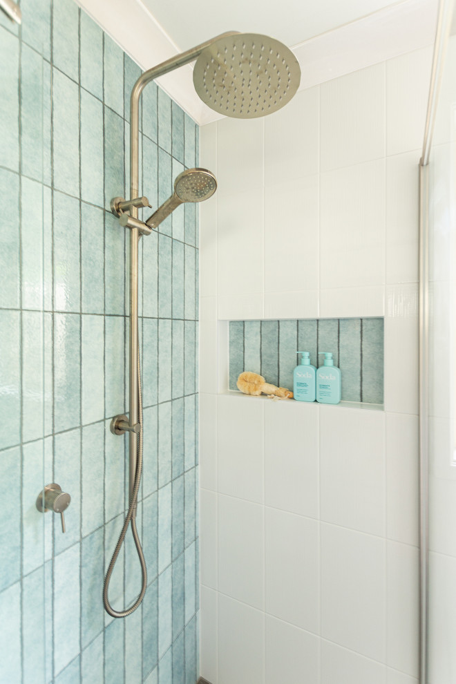 Small beach style shower room bathroom in Central Coast with flat-panel cabinets, light wood cabinets, a corner shower, a two-piece toilet, blue tiles, white walls, an integrated sink, grey floors, a hinged door, white worktops, a wall niche, a single sink and a freestanding vanity unit.