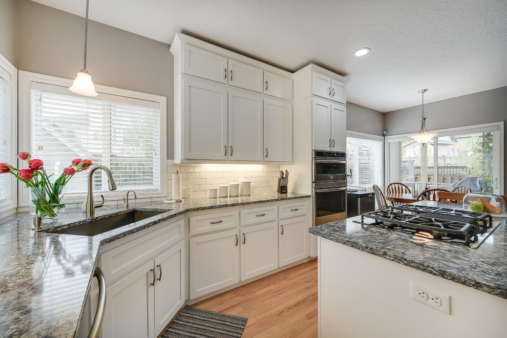 Mid-sized transitional l-shaped light wood floor and brown floor enclosed kitchen photo in Portland with a drop-in sink, shaker cabinets, white cabinets, quartz countertops, white backsplash, subway tile backsplash, an island and stainless steel appliances