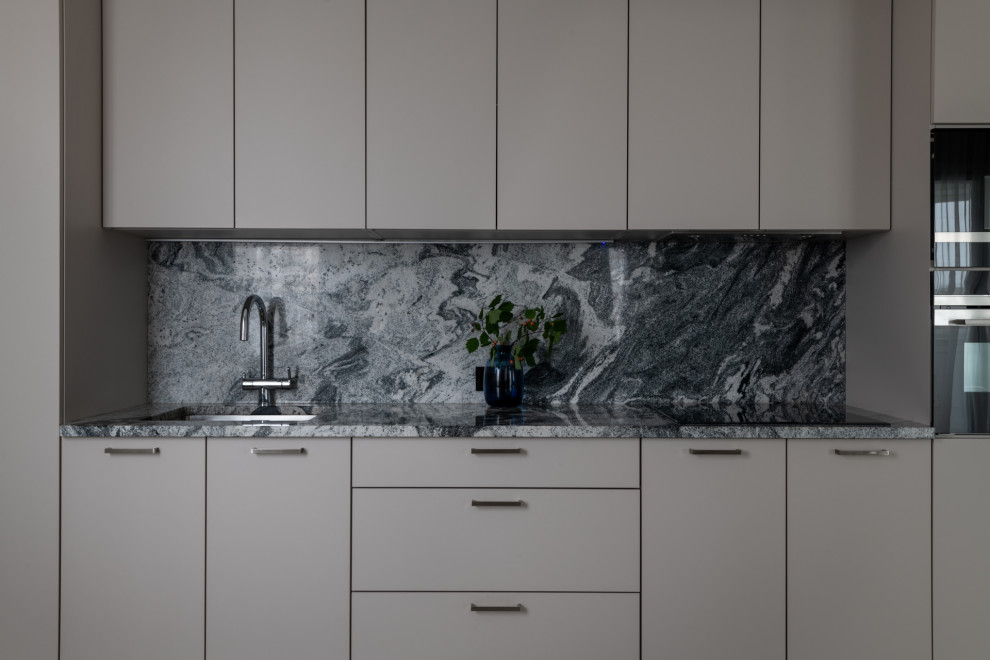 This is an example of a large contemporary single-wall open plan kitchen in Moscow with an undermount sink, flat-panel cabinets, beige cabinets, granite benchtops, grey splashback, granite splashback, black appliances, porcelain floors, no island, beige floor and multi-coloured benchtop.