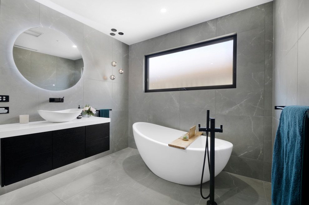 Inspiration for a contemporary master bathroom in Melbourne with flat-panel cabinets, black cabinets, a freestanding tub, gray tile, a vessel sink, grey floor, white benchtops, a single vanity and a floating vanity.