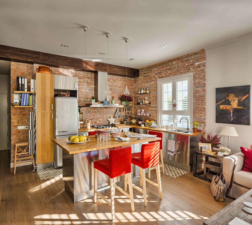 Large eclectic l-shaped open plan kitchen in Madrid with flat-panel cabinets, stainless steel cabinets, wood benchtops, medium hardwood floors and with island.