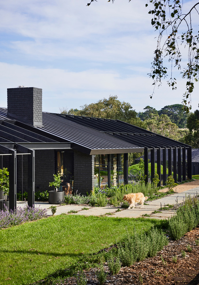 Large contemporary one-storey brick black house exterior with a gable roof, a metal roof and a black roof.