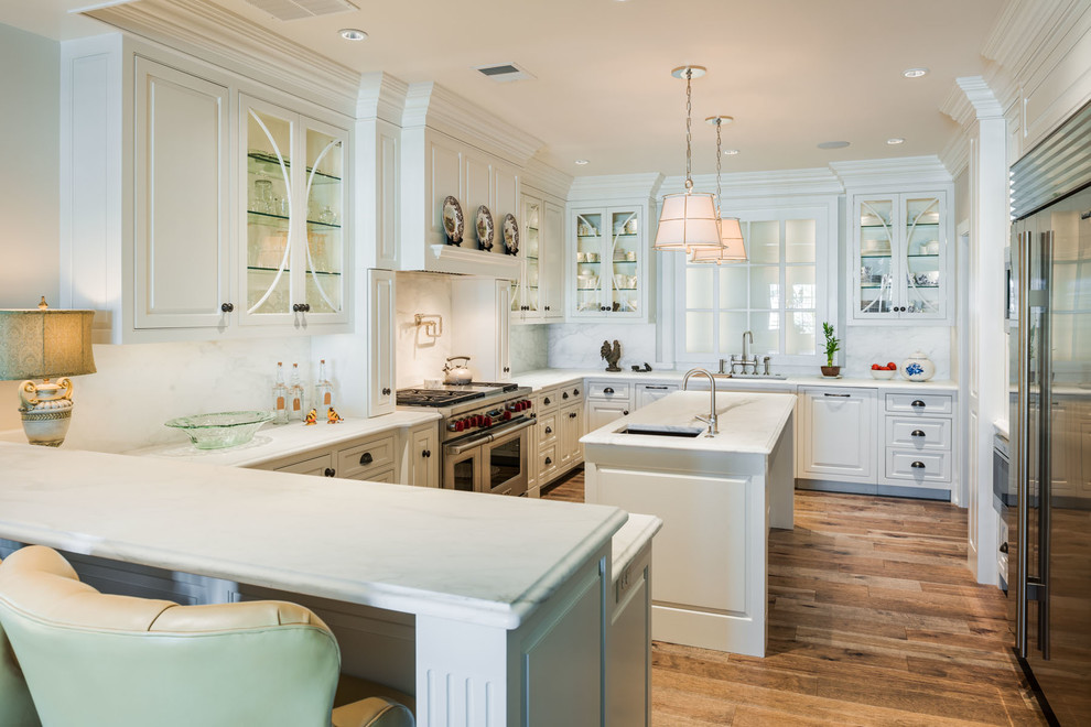 Traditional u-shaped kitchen in Philadelphia with beaded inset cabinets, white cabinets, white splashback, stainless steel appliances, medium hardwood floors and with island.