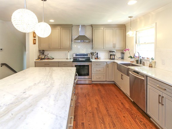 Mid-sized country l-shaped eat-in kitchen in Charlotte with a farmhouse sink, raised-panel cabinets, grey cabinets, marble benchtops, white splashback, porcelain splashback, stainless steel appliances, dark hardwood floors, with island and brown floor.