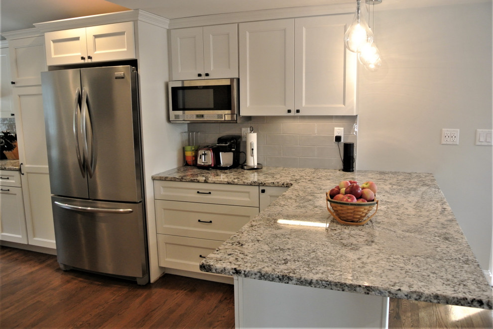 Inspiration for a transitional l-shaped medium tone wood floor and brown floor eat-in kitchen remodel in Boston with an undermount sink, shaker cabinets, white cabinets, granite countertops, beige backsplash, subway tile backsplash, stainless steel appliances, an island and beige countertops
