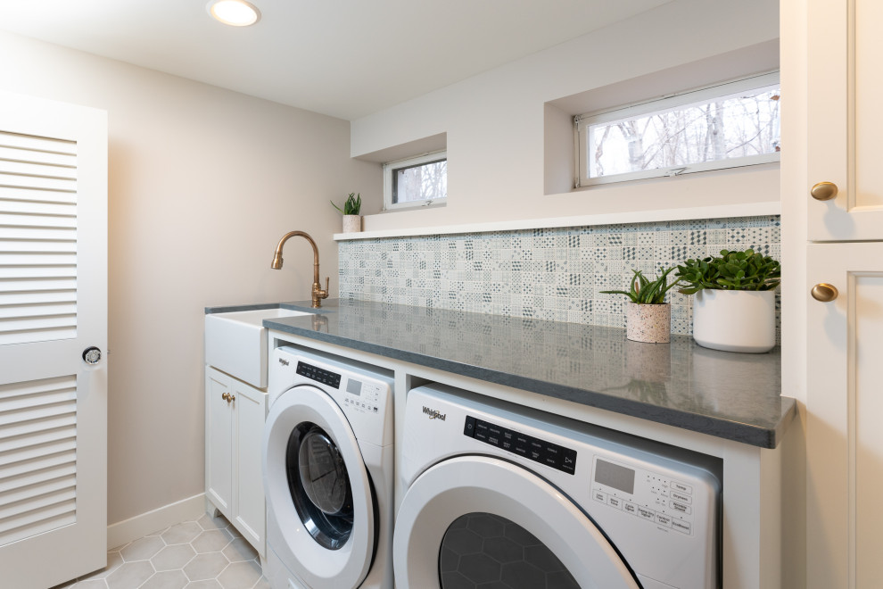 Photo of a traditional single-wall laundry room in Minneapolis with a farmhouse sink, shaker cabinets, white cabinets, beige walls, a side-by-side washer and dryer, grey floor and grey benchtop.
