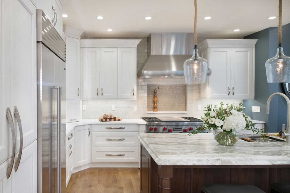 Design ideas for a transitional kitchen in Kansas City with glass-front cabinets, white cabinets, quartz benchtops, beige splashback, mirror splashback, stainless steel appliances, medium hardwood floors and with island.