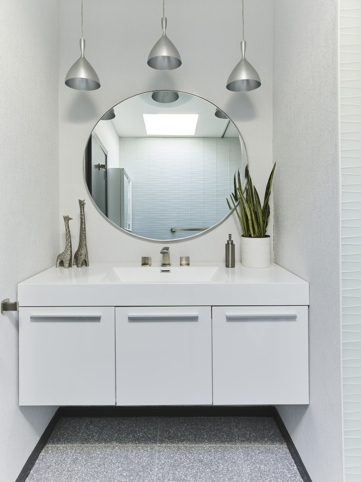 Photo of a small midcentury bathroom in Los Angeles with flat-panel cabinets, white cabinets, an alcove tub, a shower/bathtub combo, a one-piece toilet, white tile, glass tile, white walls, medium hardwood floors, a drop-in sink, solid surface benchtops, brown floor, a shower curtain, white benchtops, a single vanity, a floating vanity and wallpaper.