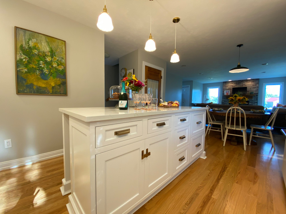 Inspiration for a mid-sized timeless l-shaped medium tone wood floor and brown floor open concept kitchen remodel in Milwaukee with a farmhouse sink, beaded inset cabinets, white cabinets, quartz countertops, white backsplash, porcelain backsplash, white appliances, an island and white countertops