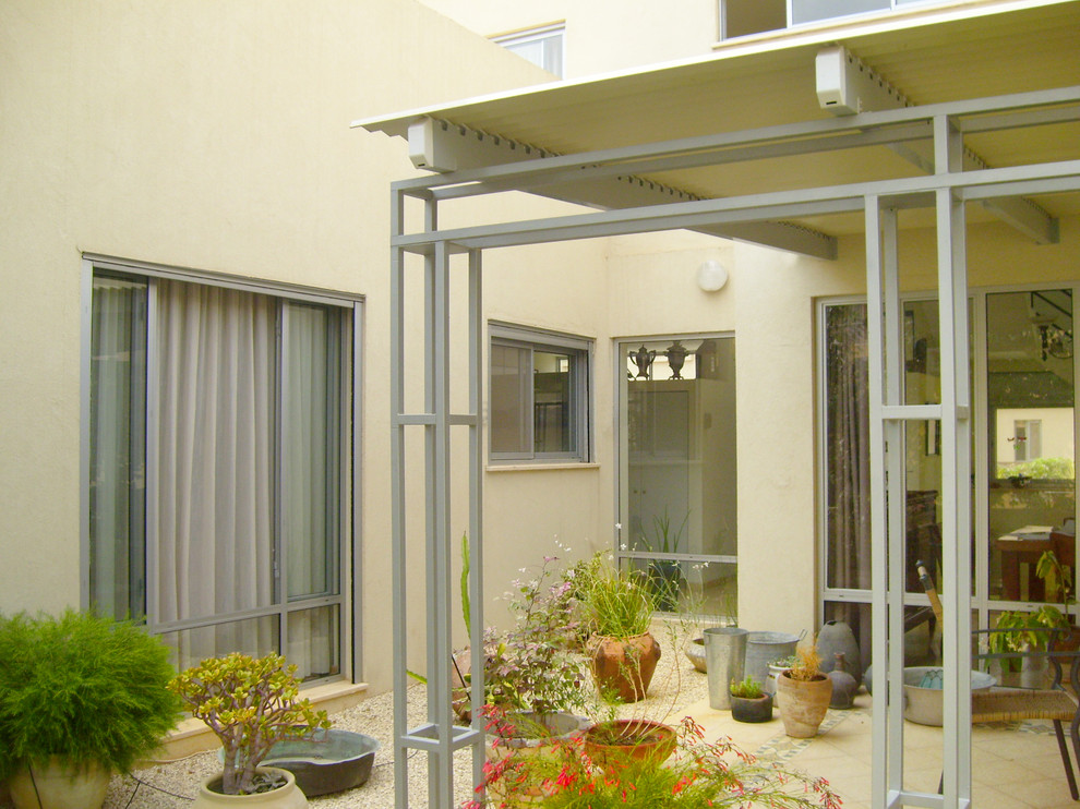 This is an example of a mid-sized mediterranean courtyard patio in Other with a container garden, gravel and an awning.